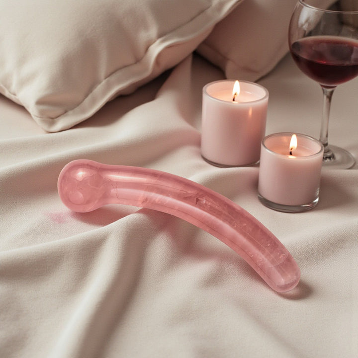 Pink crystal wand on a bed with candles and a glass of red wine.