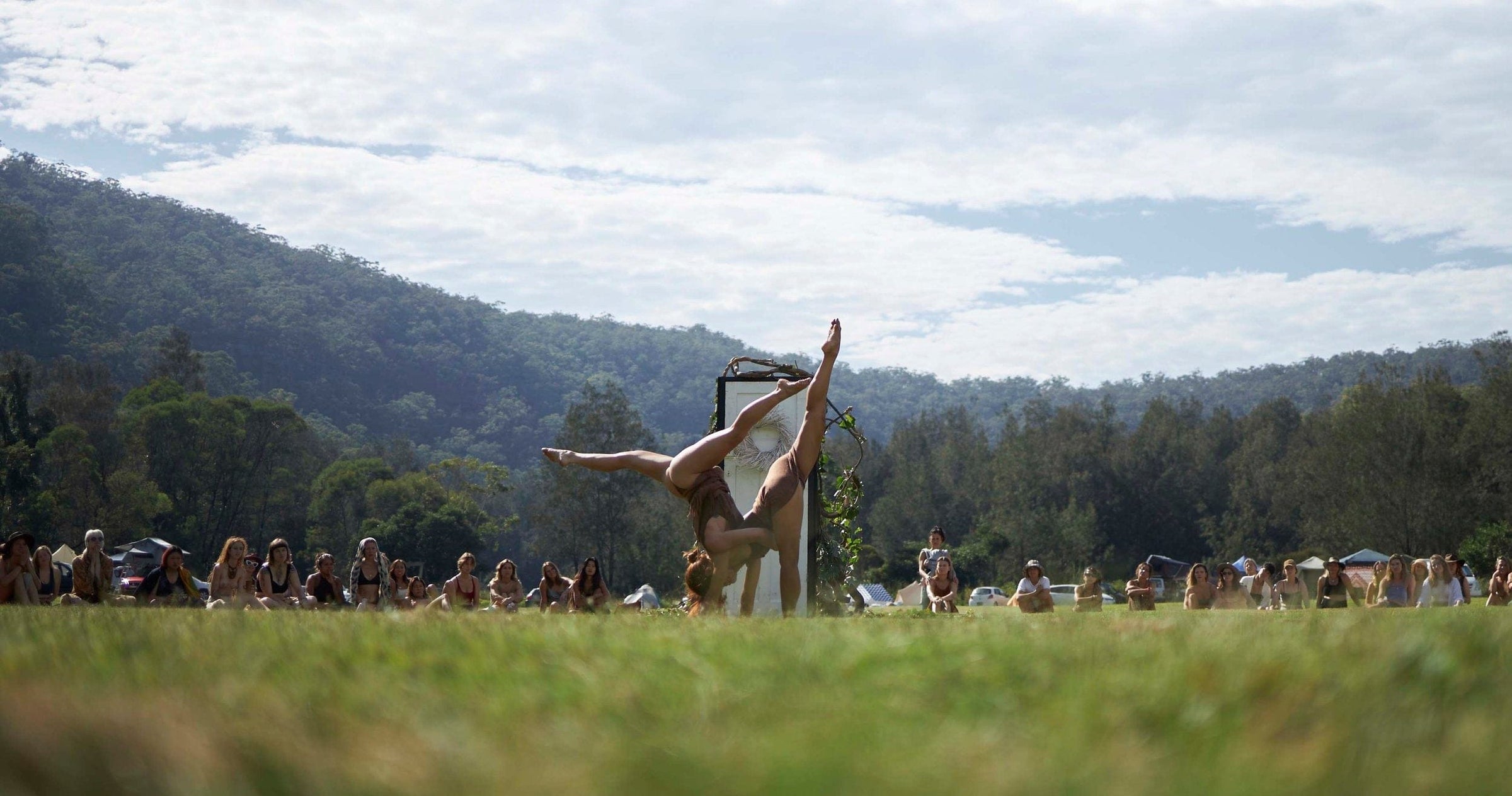 Person performing a split in a grassy field with mountains in the background. Gaiae Roots Embodiment festival 