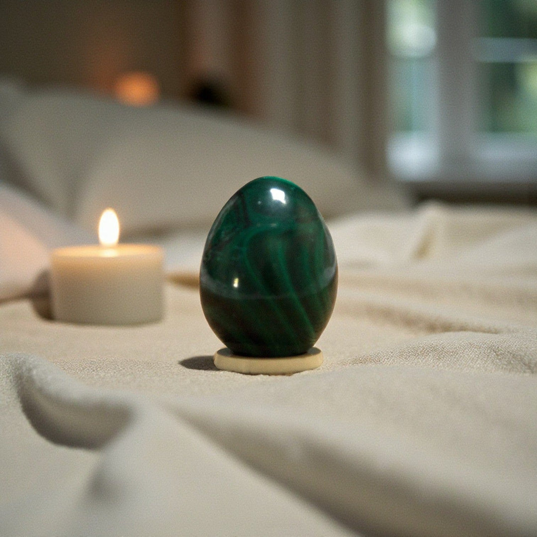 Jade Yoni Eggs on soft cream fabric next to lit candle, symbolising feminine strength and healing.