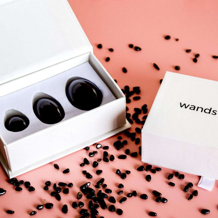 Jade yoni eggs set in a gift box with black stones on a pink background.